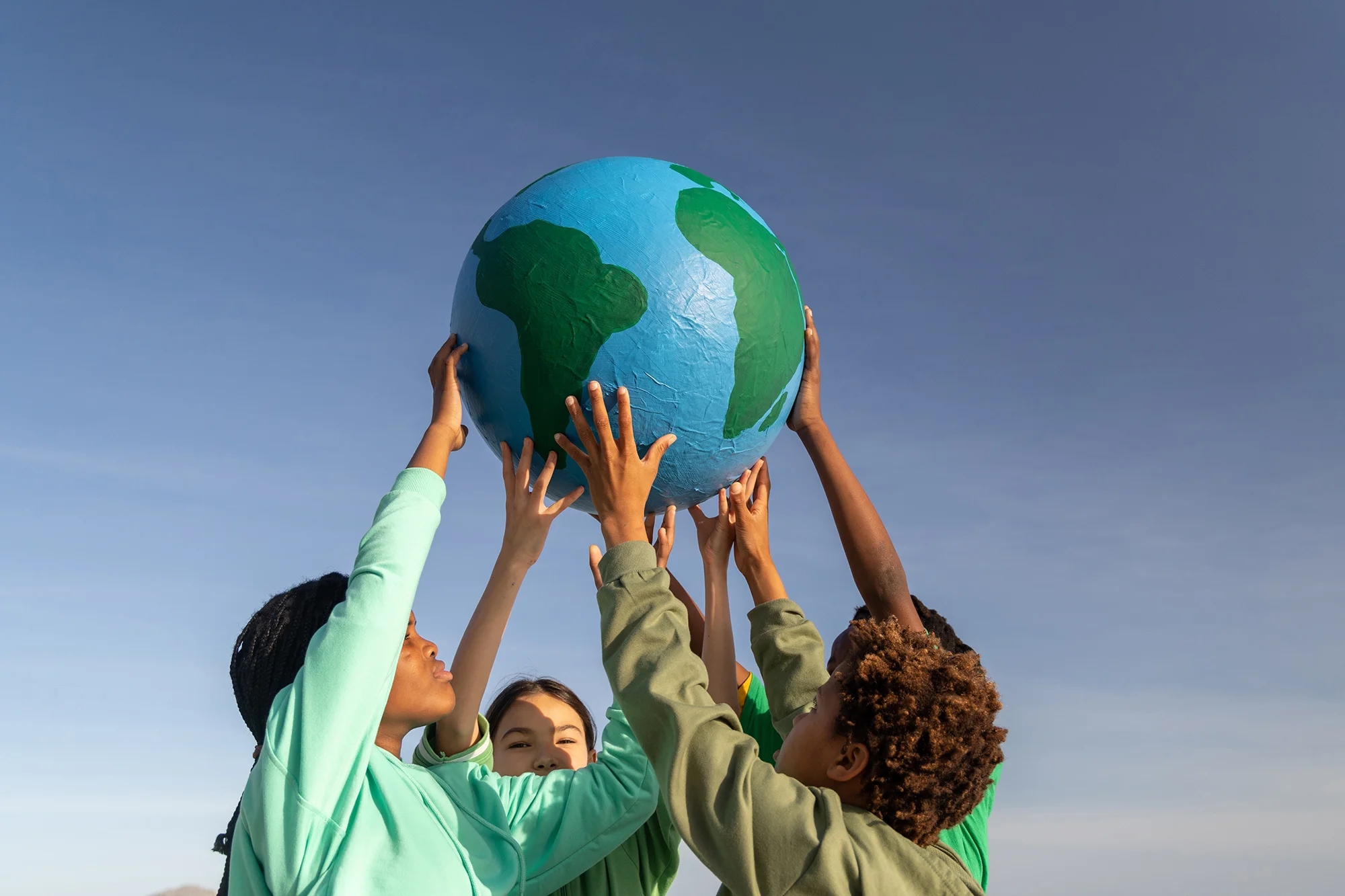 For children with their hands in the air holding a papier-mâché ball of the earth